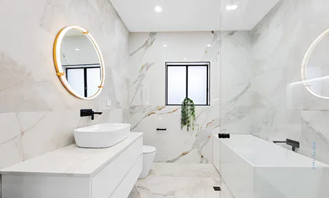 Bathroom with marble-look tiles, round backlit mirror, and pendant lighting for a soft, ambient glow.