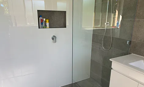 Frameless glass walk-in shower with grey stone-look tiles and brushed nickel fixtures in a modern bathroom.