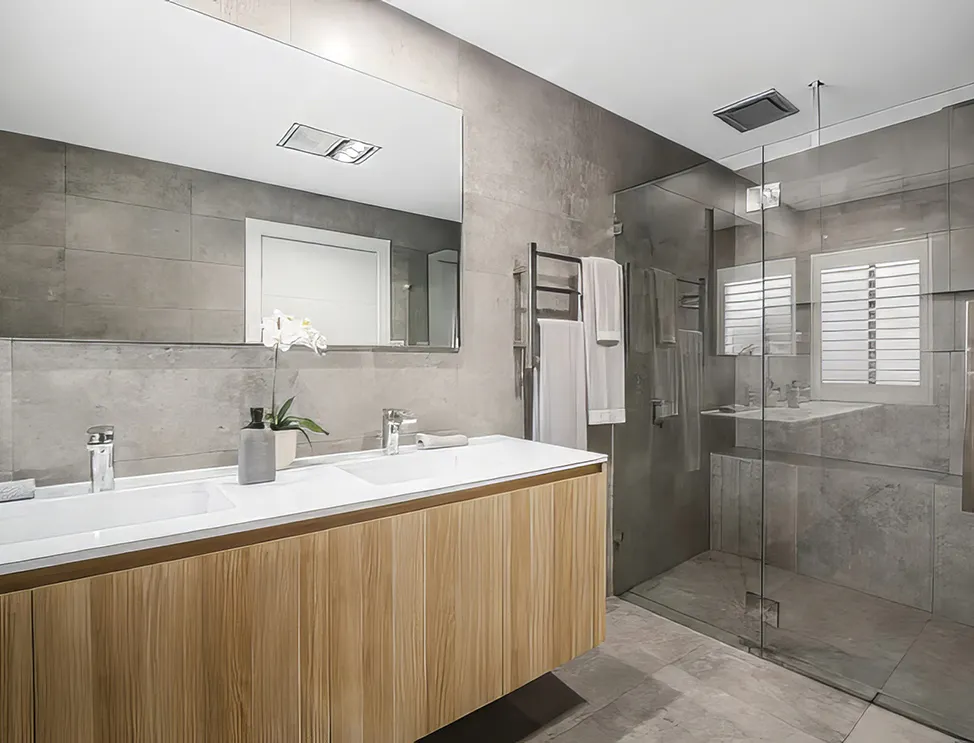 Luxury bathroom remodel featuring a floating timber double vanity with twin basins, large mirror, walk-in shower with glass enclosure, grey stone-effect tiles, heated towel rail, and modern chrome tapware.