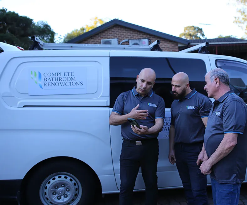 Three bathroom renovation specialists from Complete Bathroom Renovations discussing project details beside a branded white service van parked outside a suburban home in Baulkham Hills.