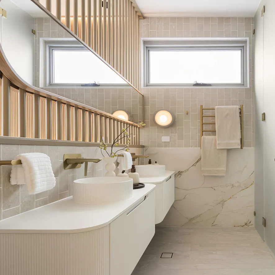 Elegant Carlingford bathroom featuring a floating vanity with ribbed detailing, beige wall tiles, marble splashback, and gold tapware under soft natural light.