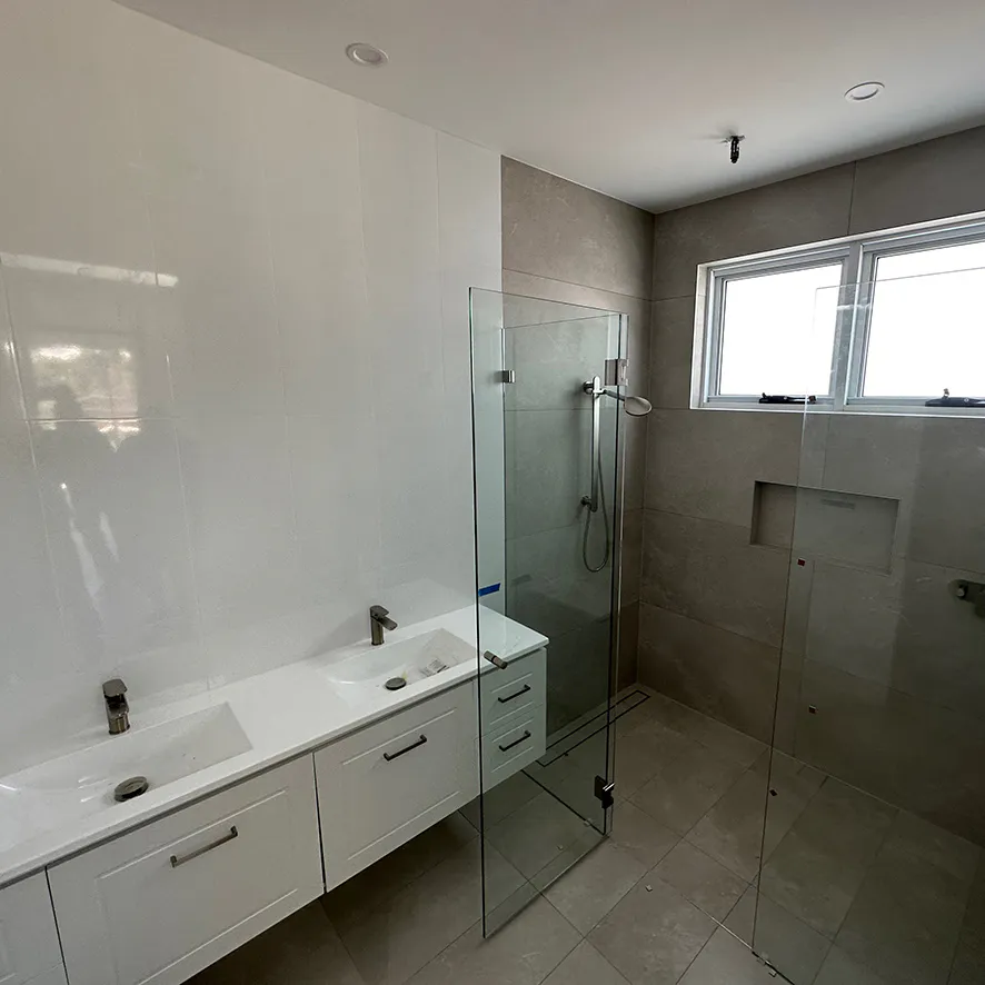 Contemporary Castle Hill bathroom renovation with frameless walk-in shower and linear drain, large grey stone-look tiles, recessed wall niche, double white vanity with integrated basins, and twin window providing natural light.