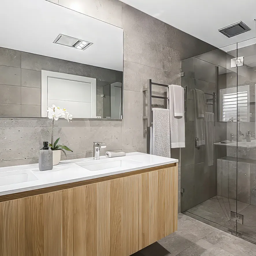 Contemporary bathroom with large grey stone tiles, frameless glass shower enclosure, double vanity with timber cabinetry and white countertop, chrome fixtures, and a wall-mounted heated towel rail for a modern, polished look.