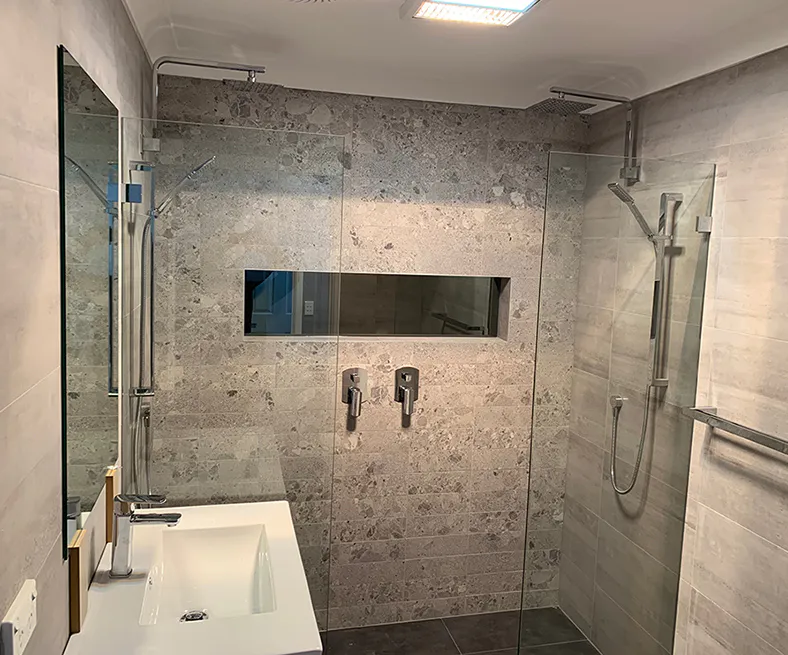 Stylish bathroom with twin rainfall showers, textured stone wall tiles, and a sleek frameless glass screen, creating a spacious and modern look.