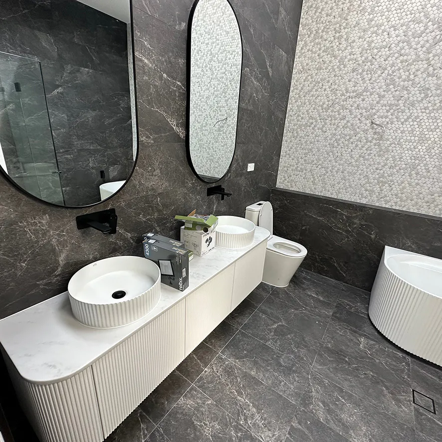 Luxury bathroom design with dark marble wall and floor tiles, fluted white double vanity and matching freestanding bathtub, round black-framed mirrors, and matte black fixtures creating a dramatic, elegant contrast.