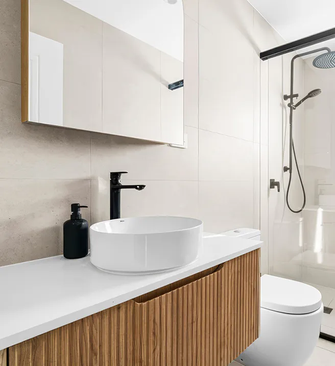 Minimalist bathroom with timber-look floating vanity, white countertop and vessel basin, black tapware, frameless glass shower enclosure, and light beige wall tiles for a clean, contemporary finish.