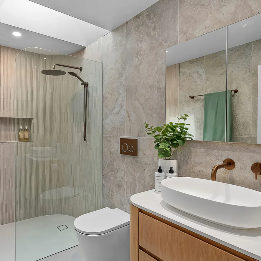 Contemporary bathroom renovation in Beecroft featuring a curved glass shower with vertical textured tiles, brushed bronze fixtures, light timber vanity, and stone-look walls for a warm, modern aesthetic.