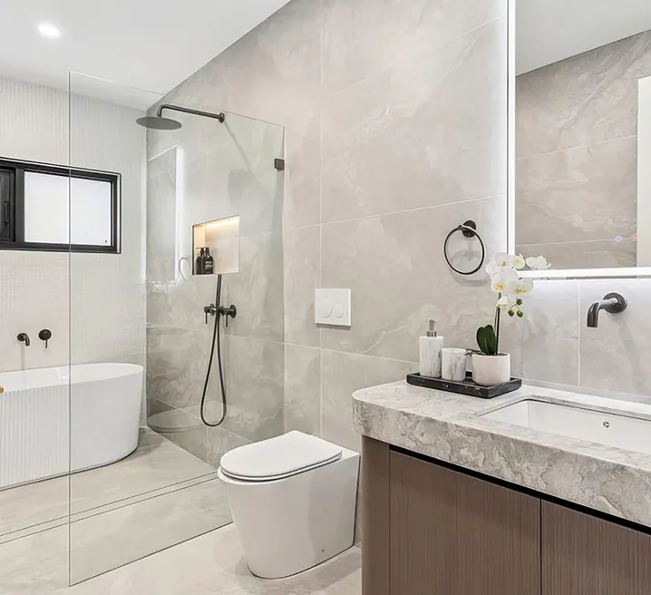 Modern bathroom featuring a freestanding fluted bathtub, grey marble-look tiles, LED-backlit mirror, wall-mounted vanity with stone benchtop, and black fixtures for a sleek, contemporary finish.