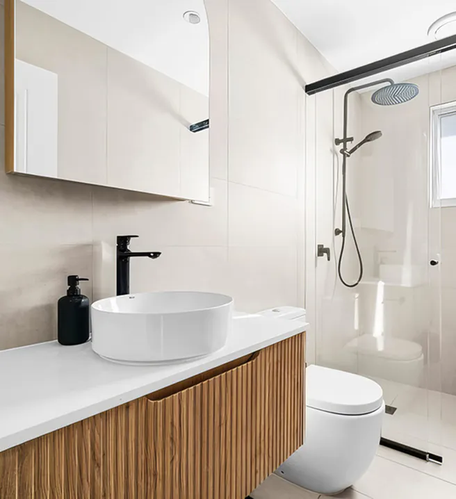 Modern bathroom with light neutral tiles, fluted timber vanity, round countertop basin, black tapware, and frameless glass shower enclosure for a clean contemporary look.