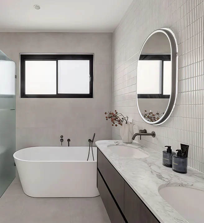 Modern bathroom renovation in Beecroft featuring a freestanding bath with fluted glass screen, marble double vanity, round backlit mirrors, and soft grey wall tiles for a refined contemporary look.