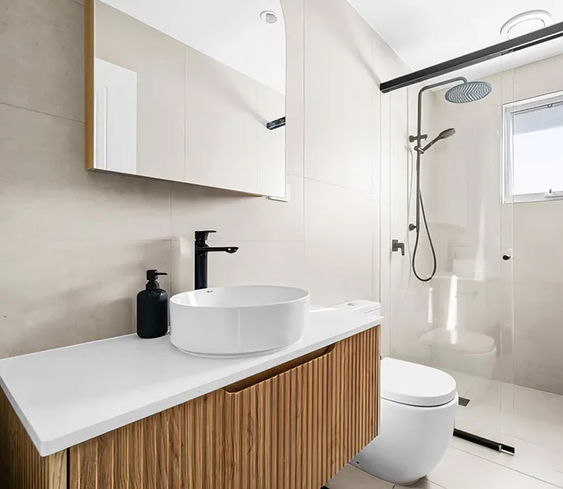 Modern bathroom renovation featuring fluted timber vanity, white countertop basin, black tapware, frameless glass shower, and light beige wall tiles for a clean, minimalist design.