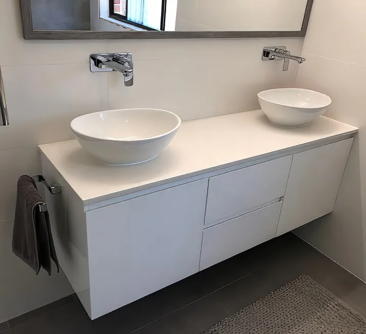 Modern bathroom featuring a sleek floating white double vanity with twin vessel basins, chrome wall-mounted taps, large mirror, stainless steel towel rail, and dark floor tiles for a clean contemporary look.