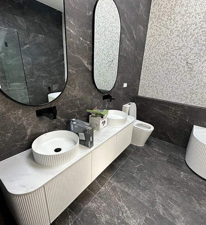 Modern Castle Hill bathroom with dark marble-look tiles, twin fluted white basins on a curved vanity, black tapware, oval mirrors, mosaic feature wall, and matching freestanding bathtub creating a luxurious contemporary look.