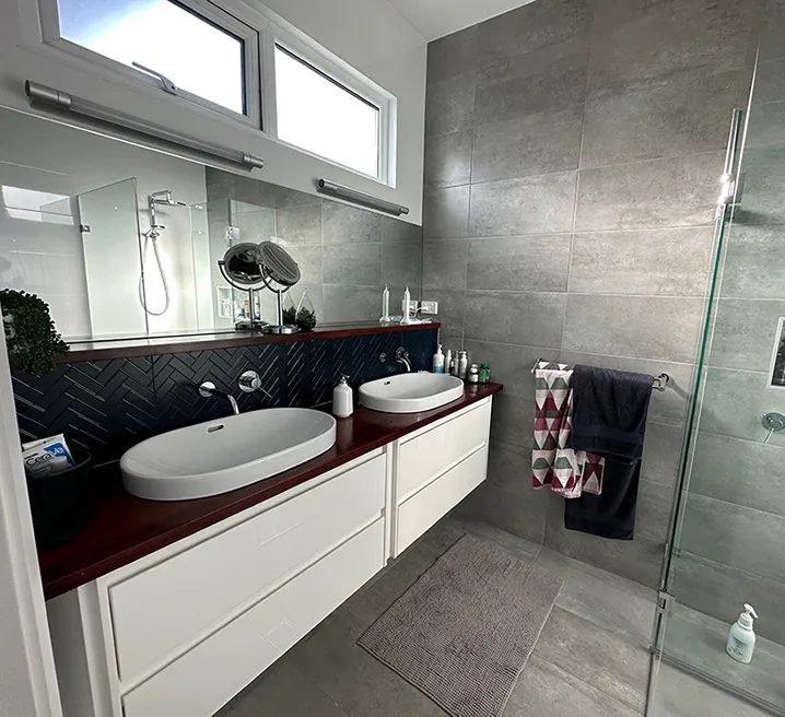 Stylish Carlingford bathroom featuring a double vanity with timber benchtop, white basins, grey tiled walls, and a glass-enclosed shower with built-in shelf.