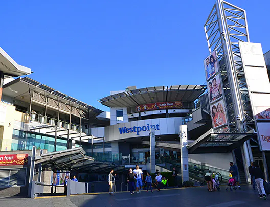 Exterior view of Westpoint Shopping Centre in Blacktown on a sunny day, showing modern architecture, glass facades, and visitors walking through the open plaza.