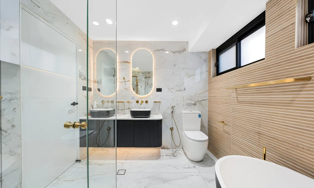 Luxurious bathroom with marble walls, modern freestanding bath, gold fixtures, and twin mirrors softly backlit — featured as the hero image for Complete Bathroom Renovations Carlingford.