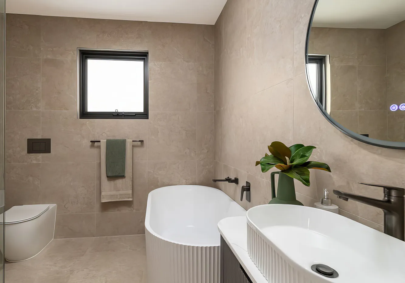 Hero image showing a modern Glenwood bathroom renovation with soft beige stone-look tiles, freestanding white bathtub, fluted vanity with vessel basin, matte black fixtures, and a circular mirror adding contrast and depth.