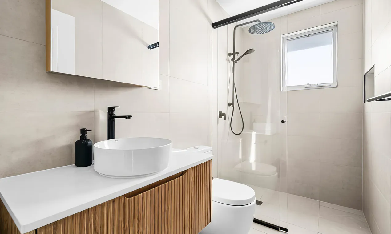 Hero image showing a modern Rouse Hill bathroom renovation with soft beige wall tiles, floating timber vanity with fluted drawers, white countertop and vessel basin, matte black tapware, and frameless glass shower enclosure for a clean, minimalist aesthetic.