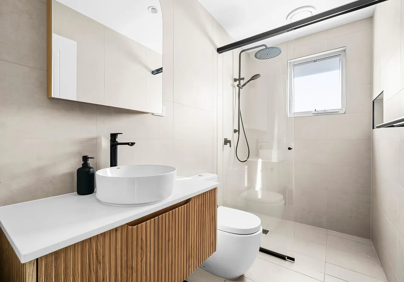 Hero image showing a modern Rouse Hill bathroom renovation with soft beige wall tiles, floating timber vanity with fluted drawers, white countertop and vessel basin, matte black tapware, and frameless glass shower enclosure for a clean, minimalist aesthetic.