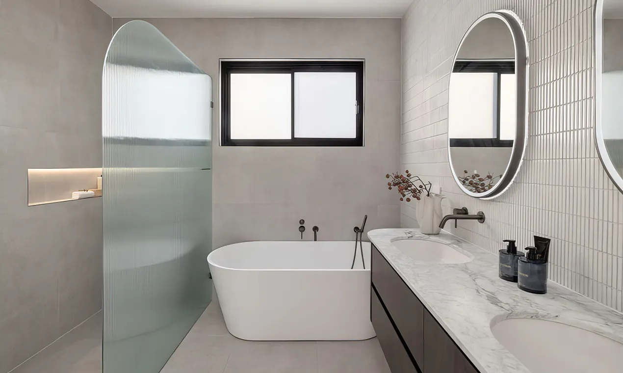 Contemporary bathroom renovation in Ryde featuring a freestanding white bath beside a fluted glass shower screen, twin backlit mirrors above a marble vanity, matte black tapware, and soft grey wall tiles for a clean, minimalist aesthetic.