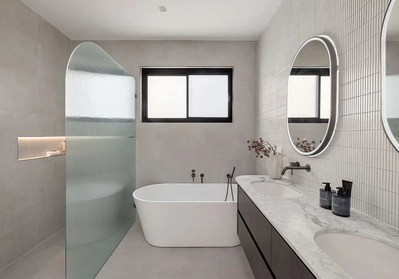 Contemporary bathroom renovation in Ryde featuring a freestanding white bath beside a fluted glass shower screen, twin backlit mirrors above a marble vanity, matte black tapware, and soft grey wall tiles for a clean, minimalist aesthetic.